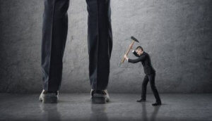 Small businessman hitting giant legs of another with hammer