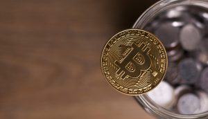 Bitcoin-Münze liegta auf dem Rand eines Glases voller Kleingeld