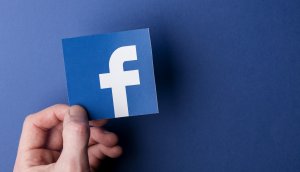 Das Facebook-Symbol von einer Hand gehalten auf blauem Hintergrund