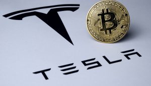 Ein Bitcoin neben dem Logo des US-Autobauers Tesla.