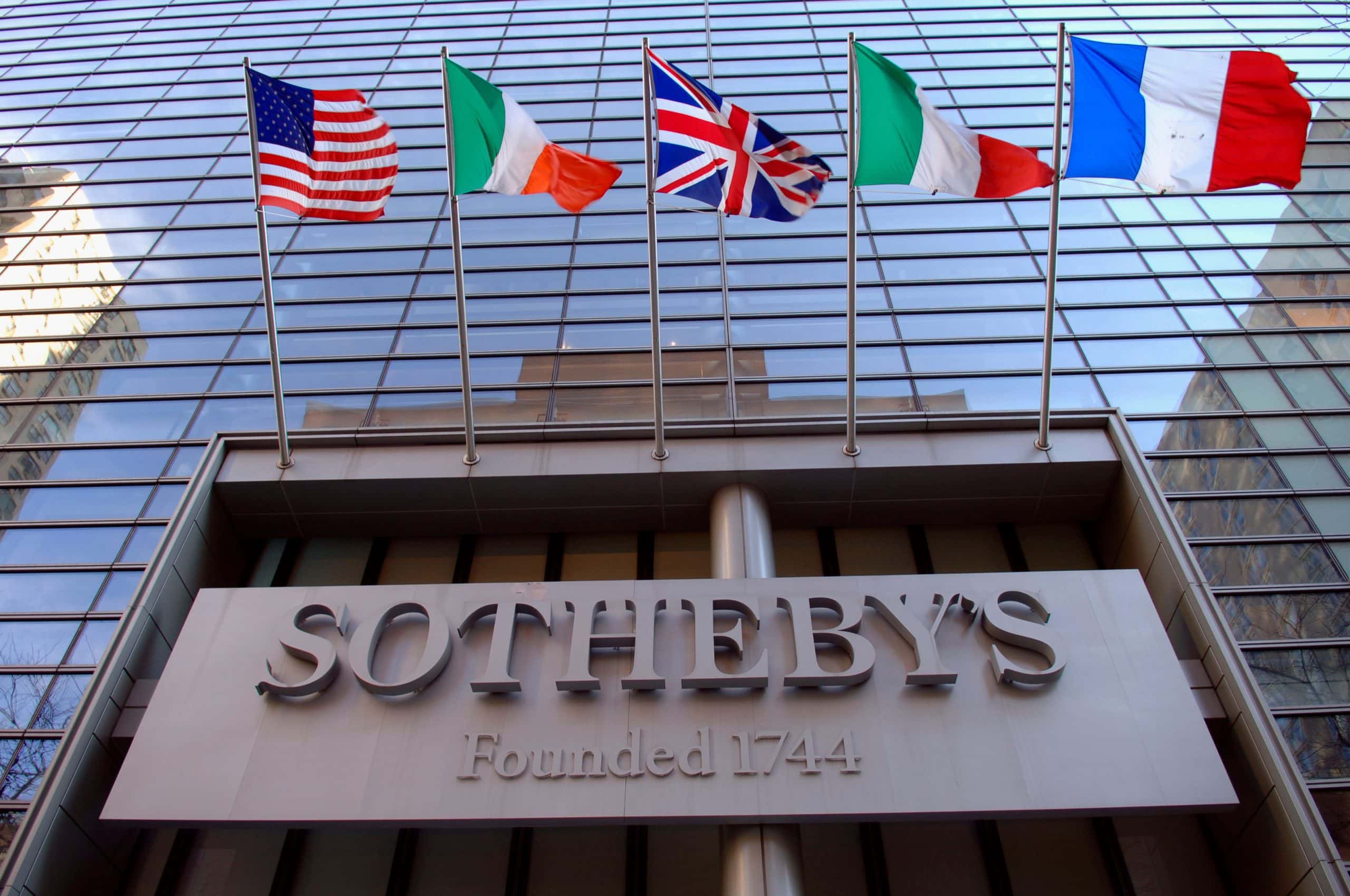 Das Sotheby's-Logo prangt an einer gläsernen Fassade. Darüber wehen die Flaggen der USA, Italiens, Großbritanniens, Irlands und Frankreichs.