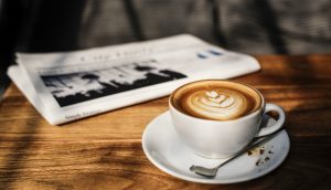Eine Zeitung und eine Tasse Kaffee stehen auf einem Holztisch.