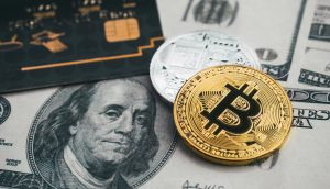 Eine Debitkarte liegt neben zwei Krypto-Münzen auf einem Hundertdollarschein.