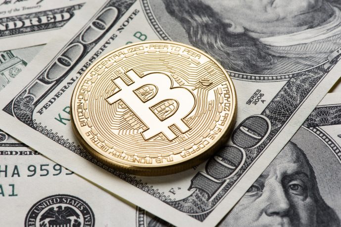 Ein Bitcoin liegt auf einer 100-US-Dollar Note.