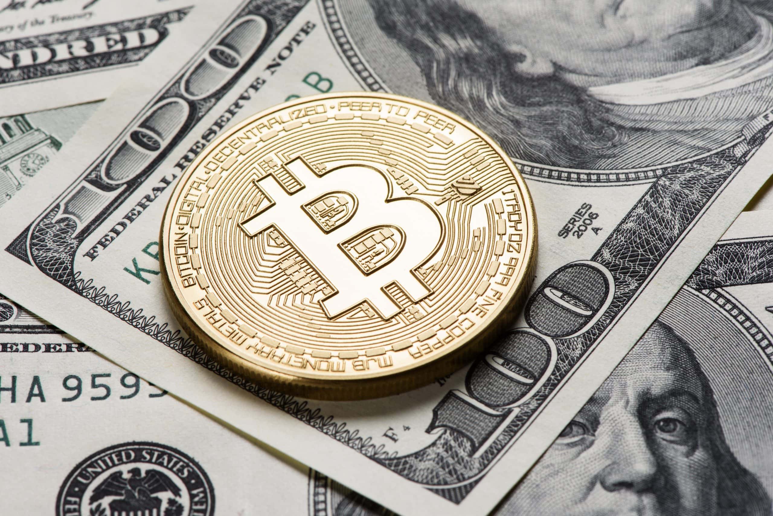 Ein Bitcoin liegt auf einer 100-US-Dollar Note.