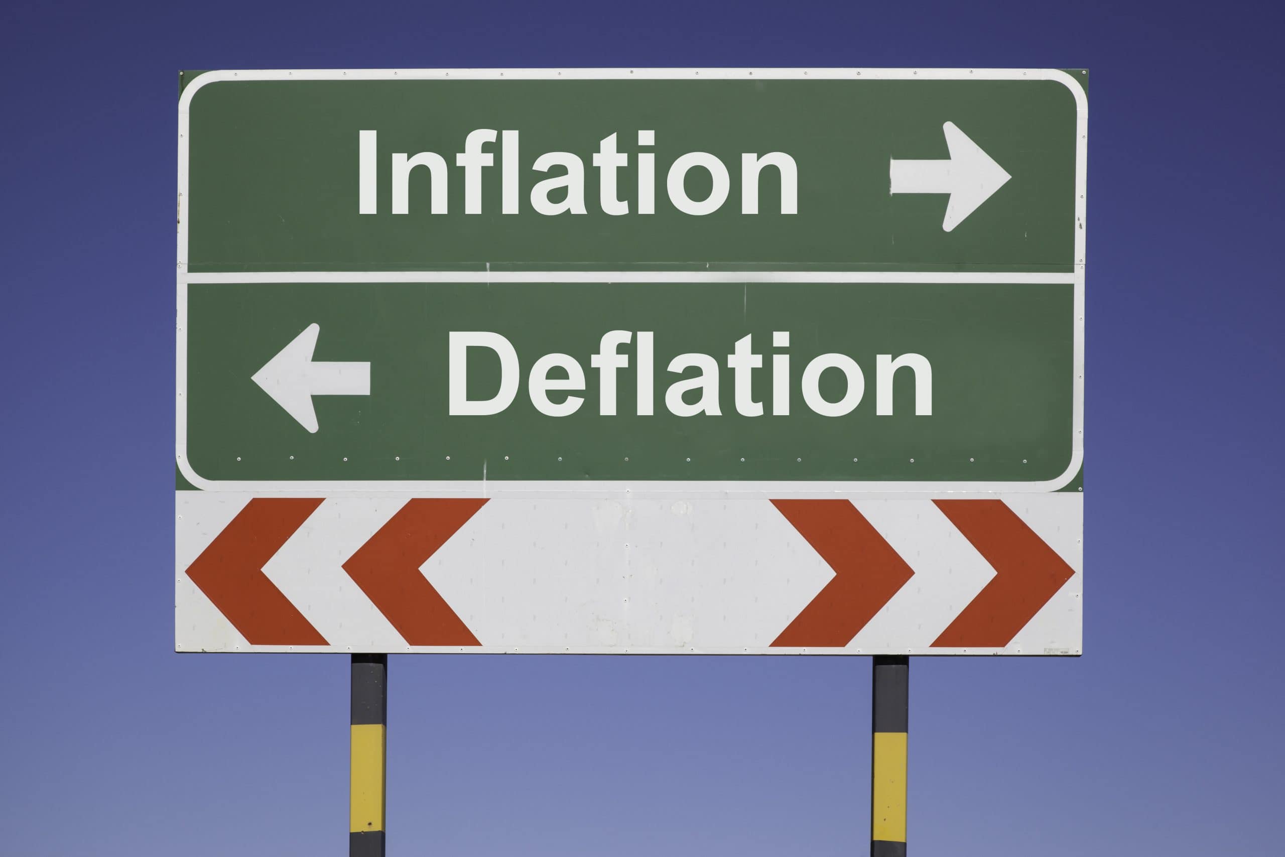 Schild gegen blauen Himmel. Nach links wird Deflation, nach rechts Inflation ausgewiesen.